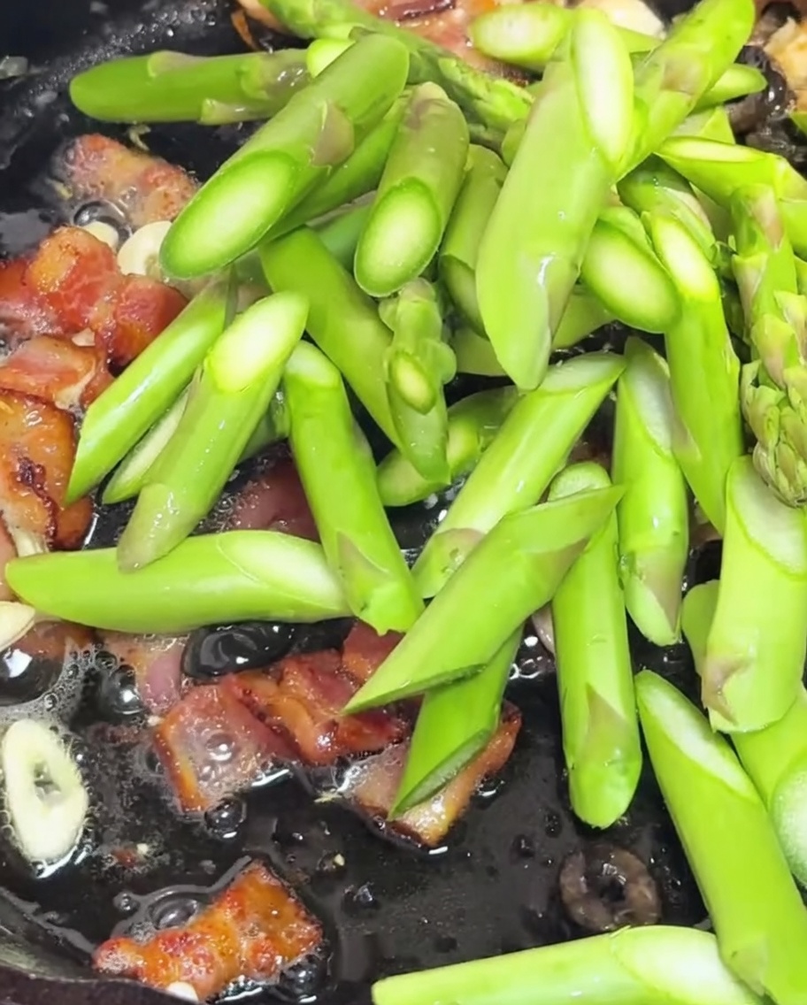 Pezzi di asparagi e pomodorini saltati in padella con bacon e aglio.