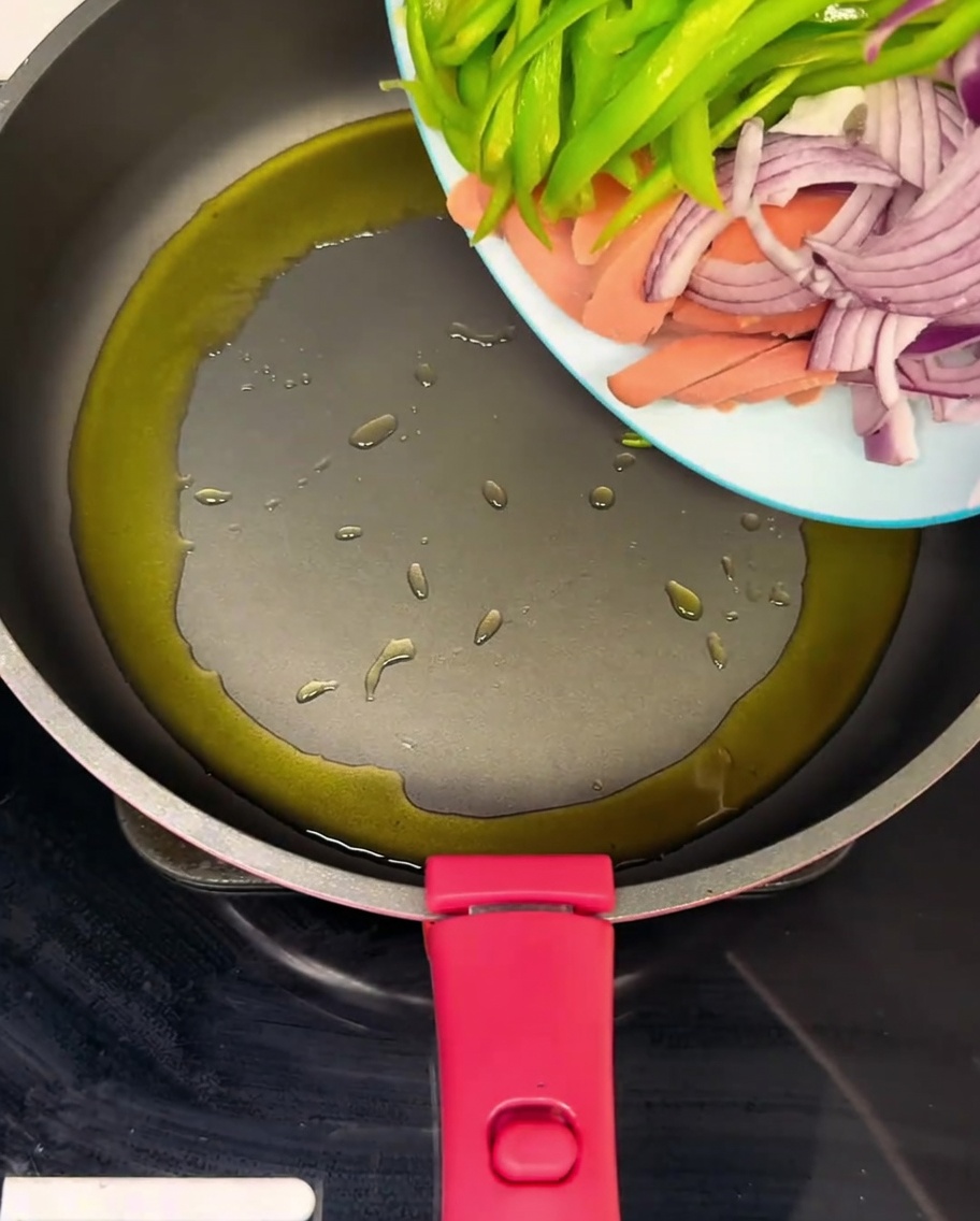 Una padella calda contenente prosciutto a fette, peperoni verdi e cipolle saltati nellolio.