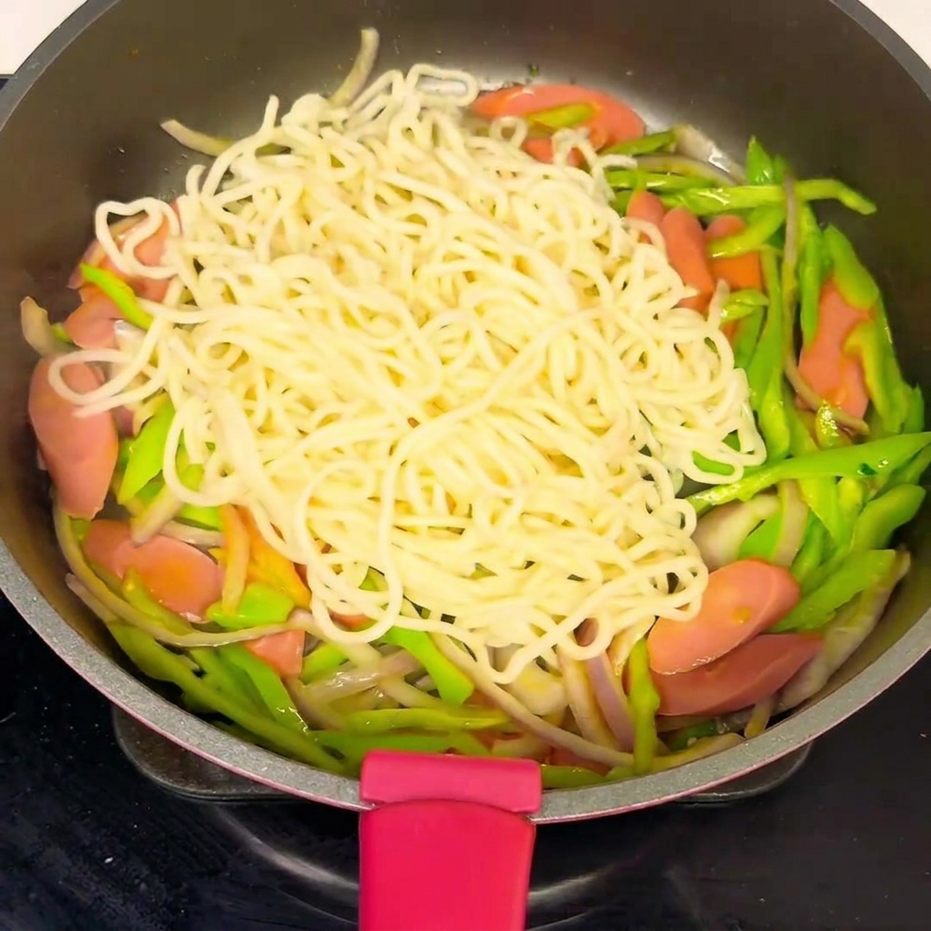 Una padella piena di noodles e verdure, con una salsa versata sopra il composto.