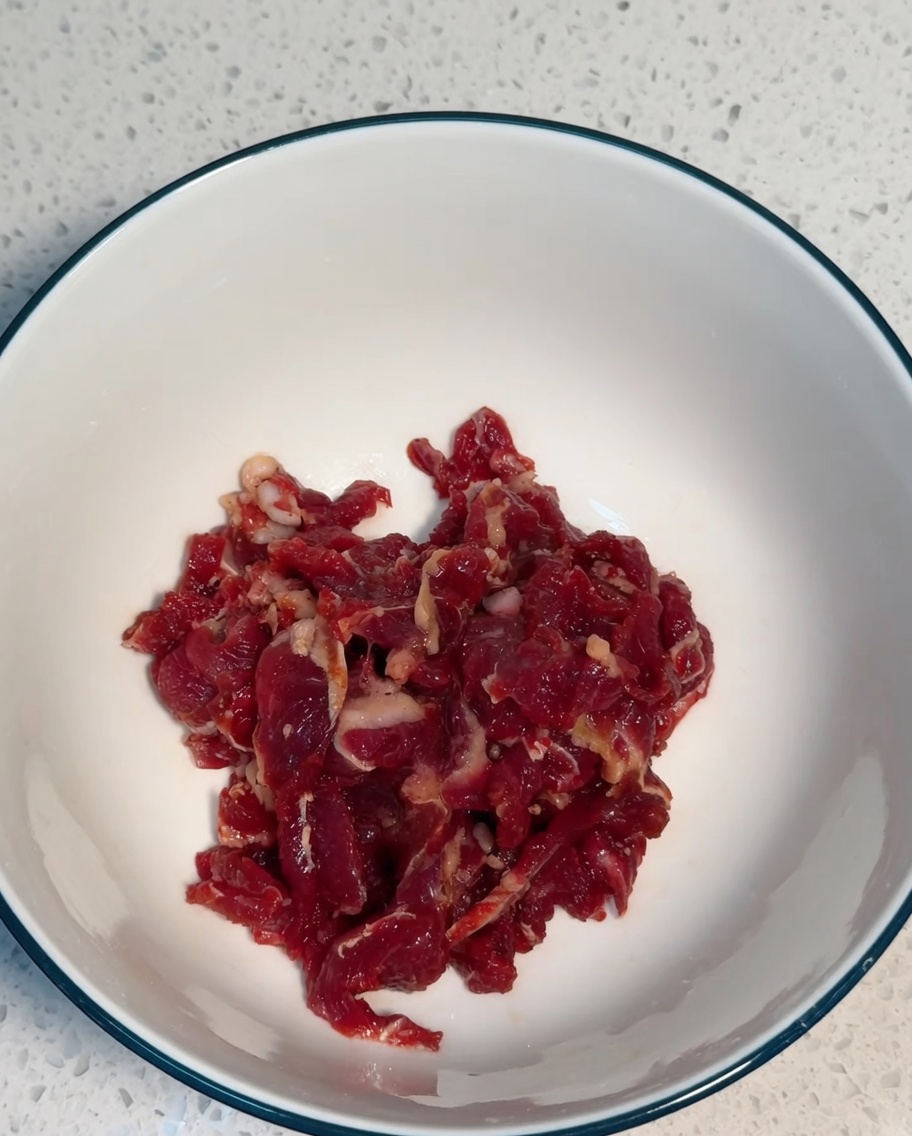 Straccetti di manzo mescolati con gli ingredienti della marinatura in una ciotola bianca.