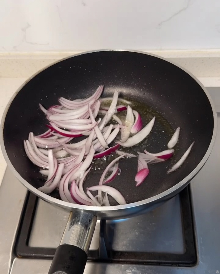 Pezzi di cipolla viola che sfrigolano in padella con olio caldo.