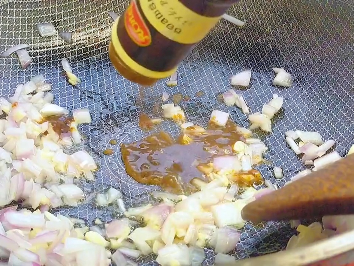 Salsa al pepe nero versata da una bottiglia in un wok sopra gli aromi saltati.