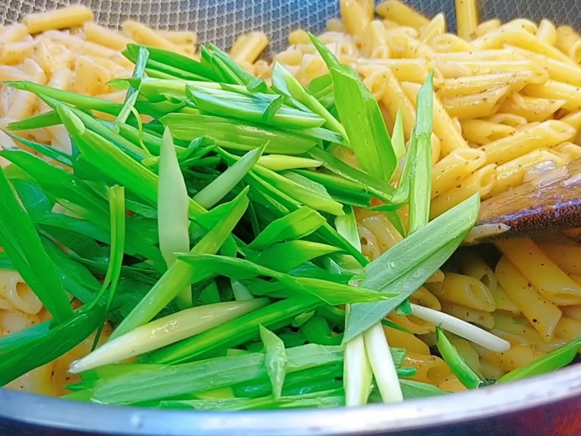 Germogli daglio verde freschi aggiunti in un wok pieno di penne e salsa al pepe nero.