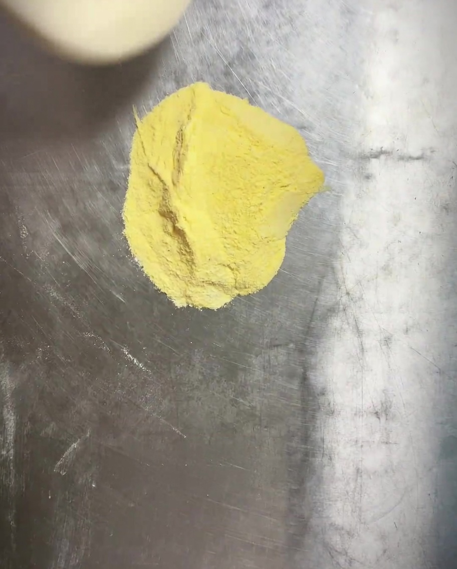 Impasto della pizza pressato in una teglia rotonda con uno strato visibile di farina di mais sul fondo.