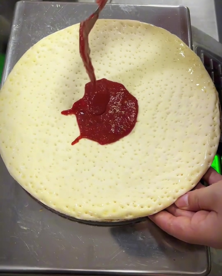 Salsa di pomodoro stesa sullimpasto usando il dorso di un cucchiaio di metallo.