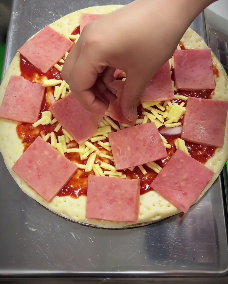 Primo piano di una pizza condita con chicchi di mais, fette di peperone verde e funghi sparsi sul prosciutto.