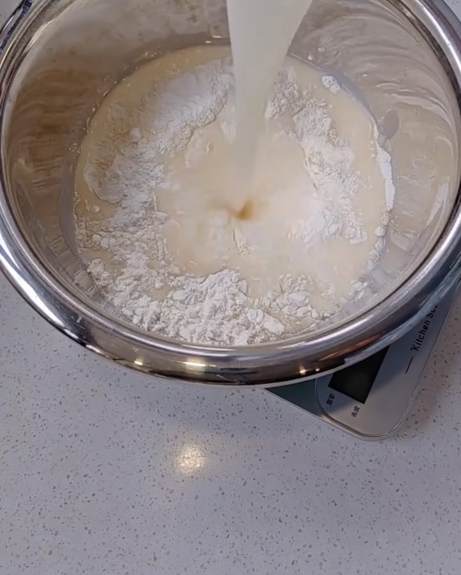 Versamento di una miscela lattiginosa di lievito e acqua da un bicchiere di vetro in una ciotola dacciaio con farina bianca.