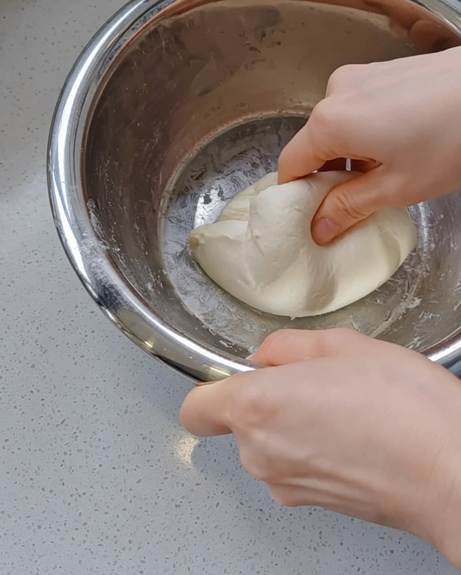 Mani che arrotondano gentilmente una palla dimpasto liscia allinterno di una ciotola dacciaio.