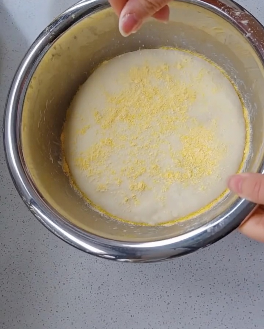 Una mano cosparge farina di mais gialla su una palla dimpasto ben lievitata e gonfia allinterno di una ciotola.