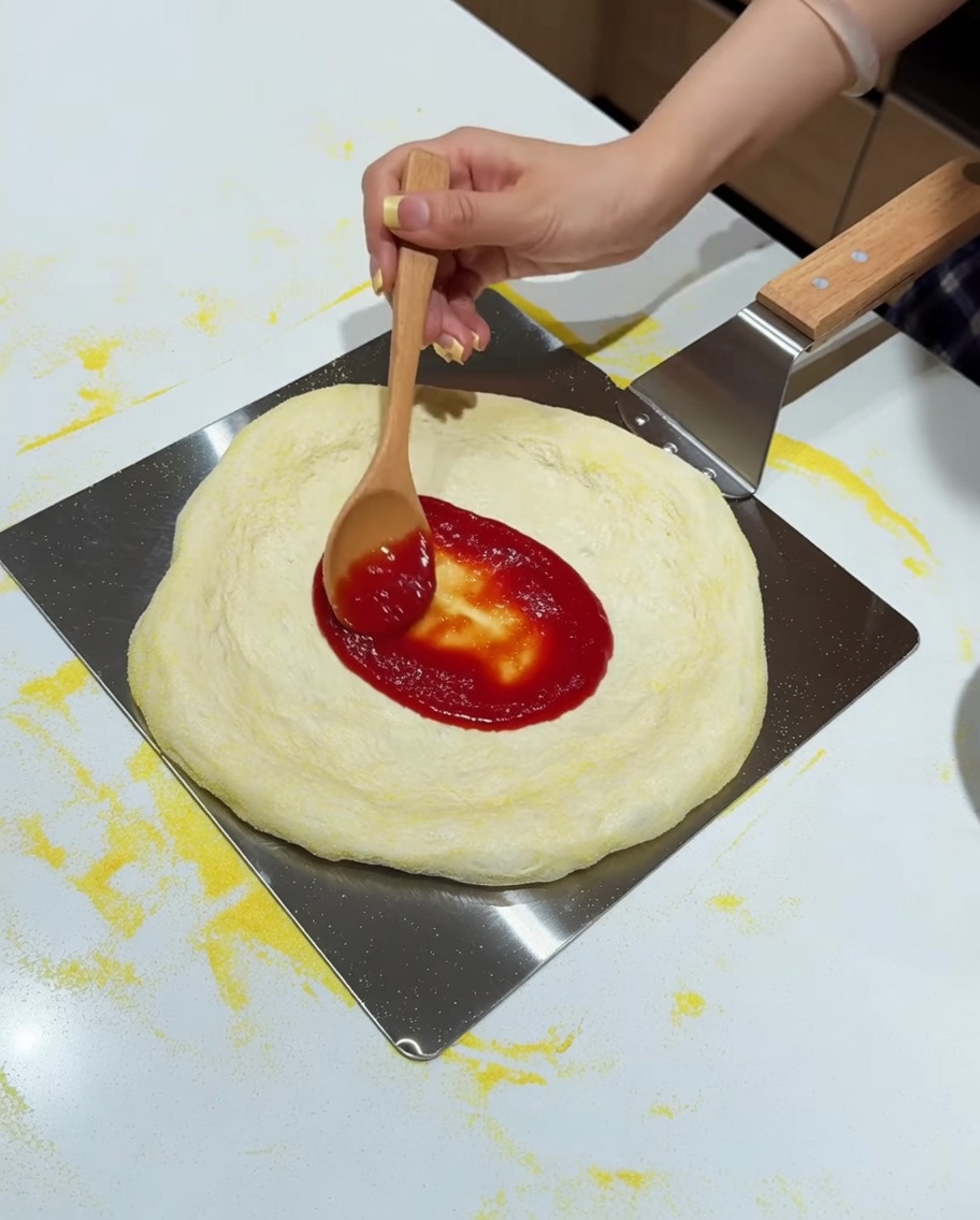 Salsa di pomodoro che viene stesa sulla pizza con un cucchiaio.
