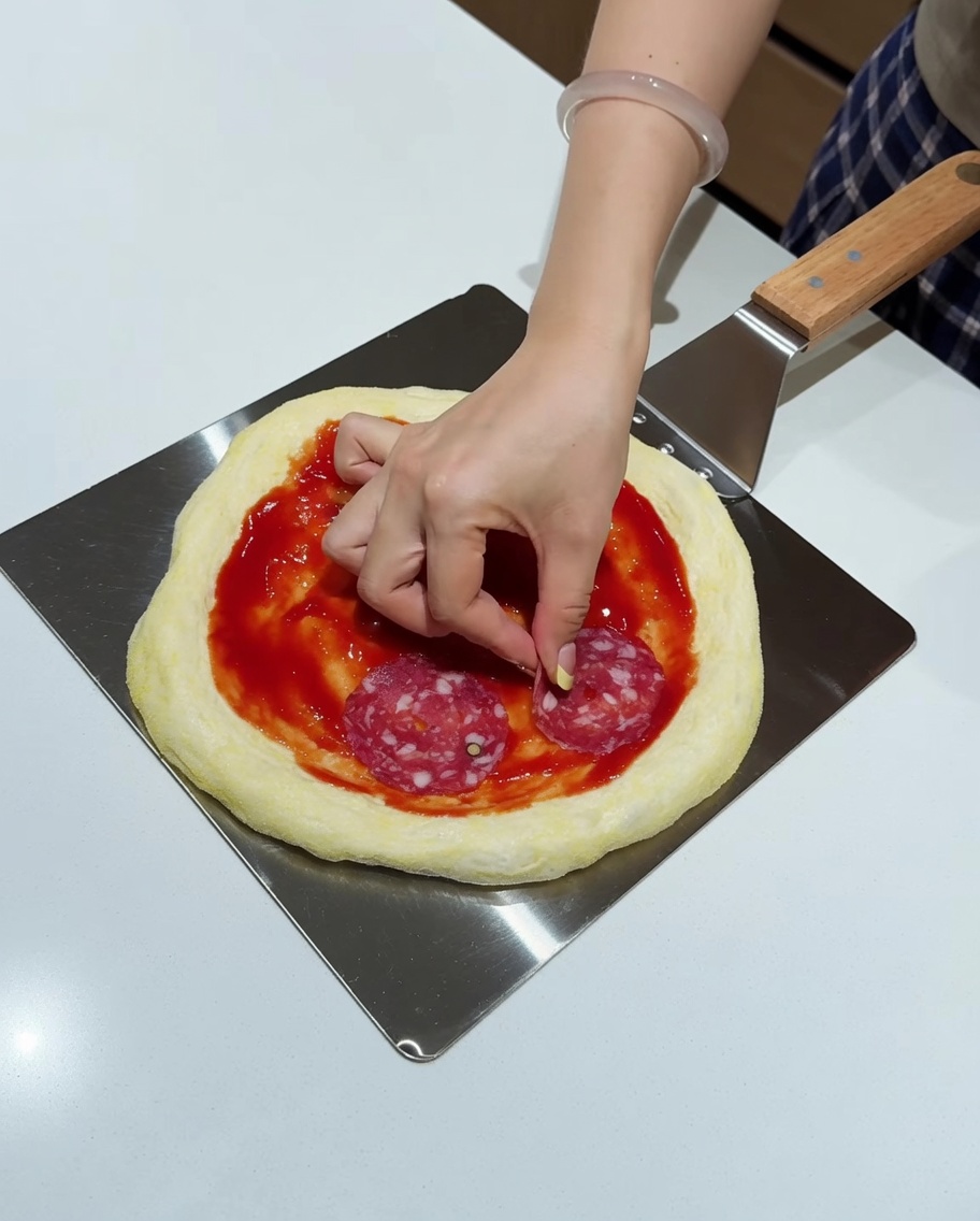 Disposizione delle fette di salame sulla pizza già condita.