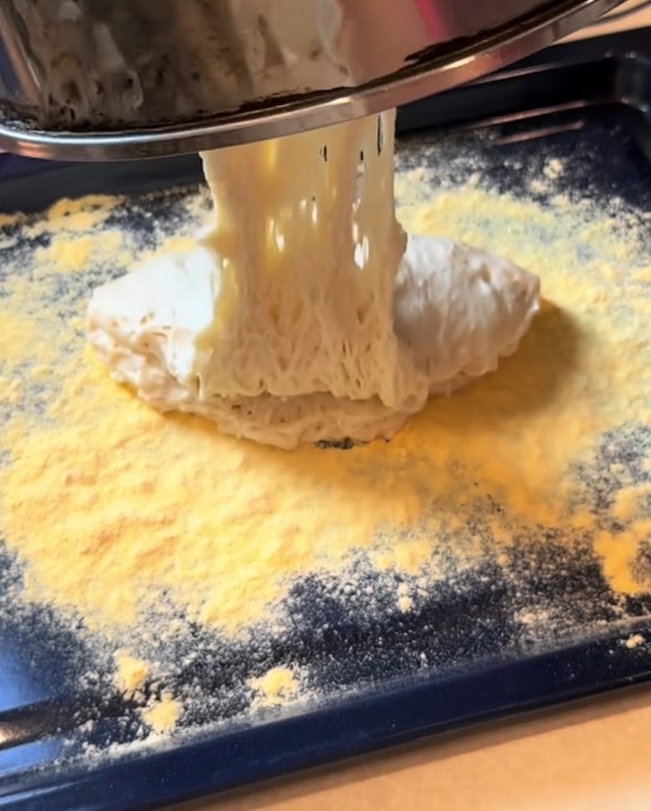 Impasto per pizza fermentato mentre viene steso in una base rettangolare su una teglia da forno.