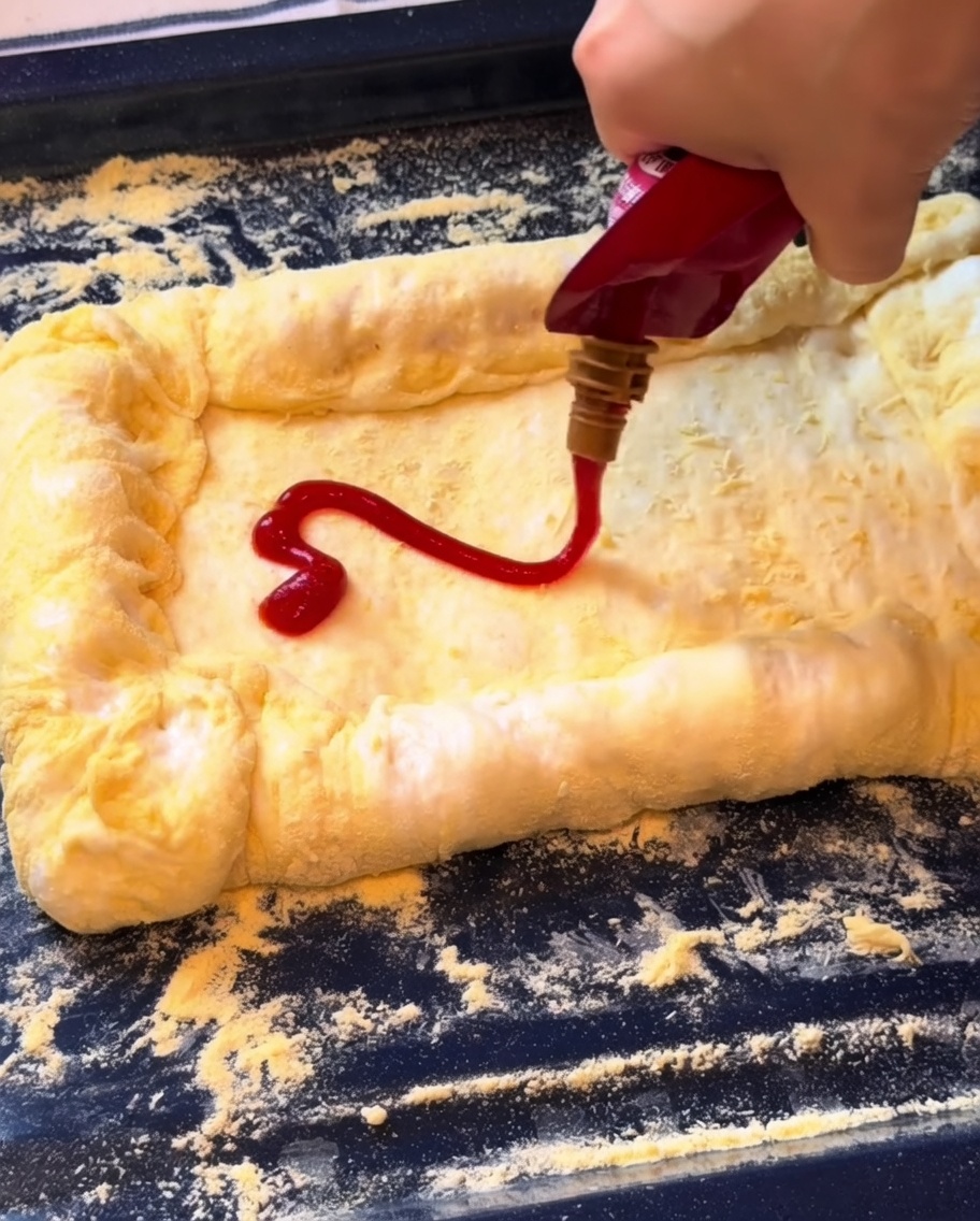 Ketchup spalmato sulla base della pizza seguito da uno strato di mozzarella grattugiata.