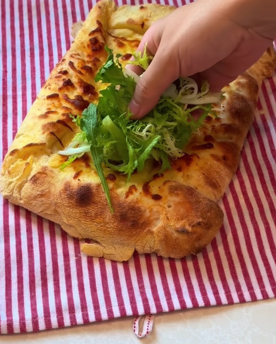 Verdure a foglia e prosciutto crudo a fette sottili posizionati sulla crosta della pizza cotta.