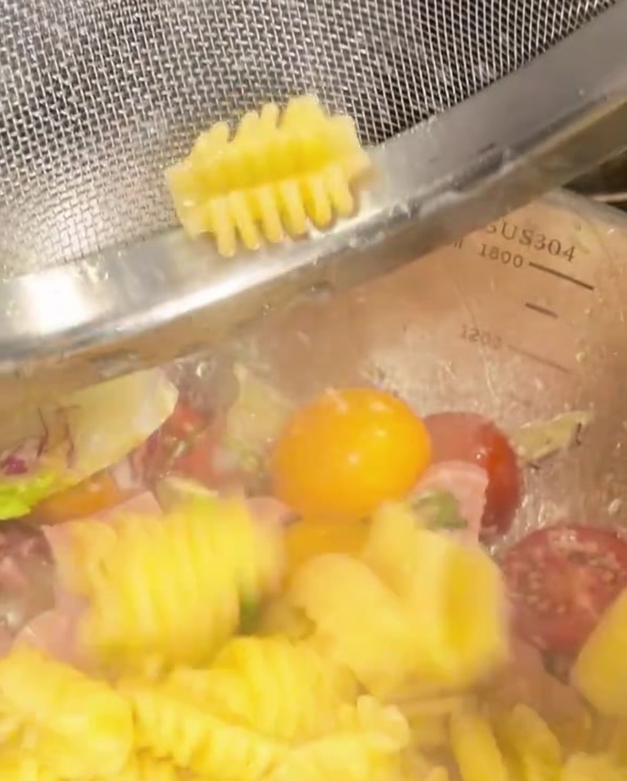 Fusilli cotti versati in una ciotola con verdure e prosciutto.