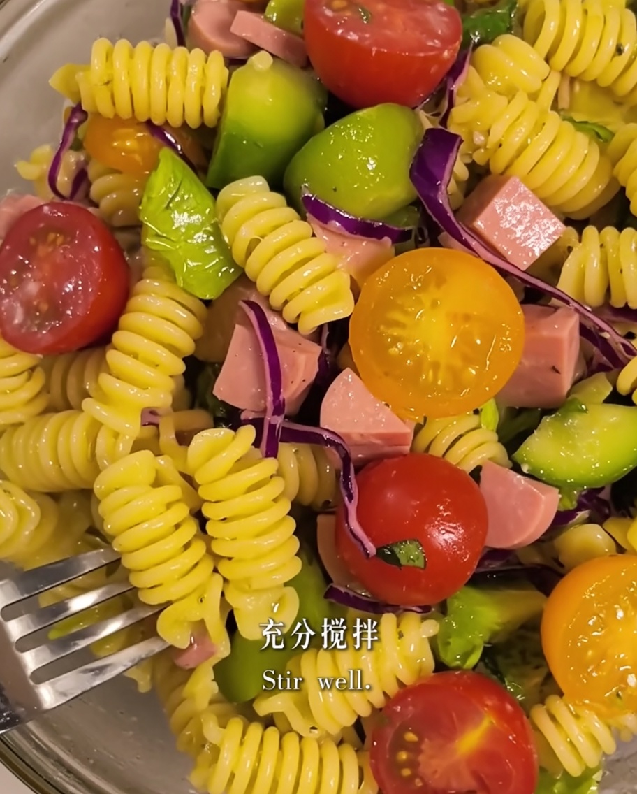Pasta e ingredienti dellinsalata mescolati insieme con olio doliva in una ciotola.