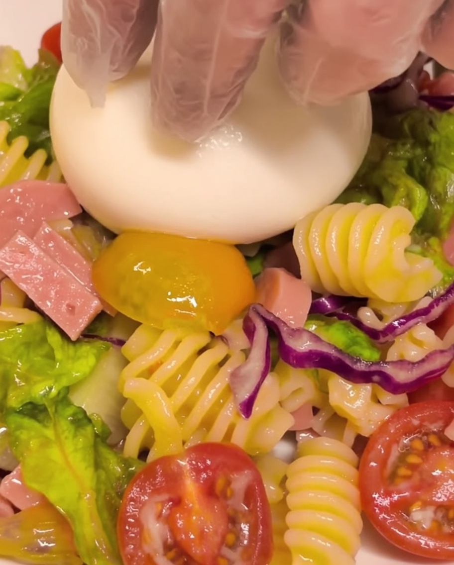 Una burrata fresca intera posizionata al centro di una porzione di insalata di pasta.
