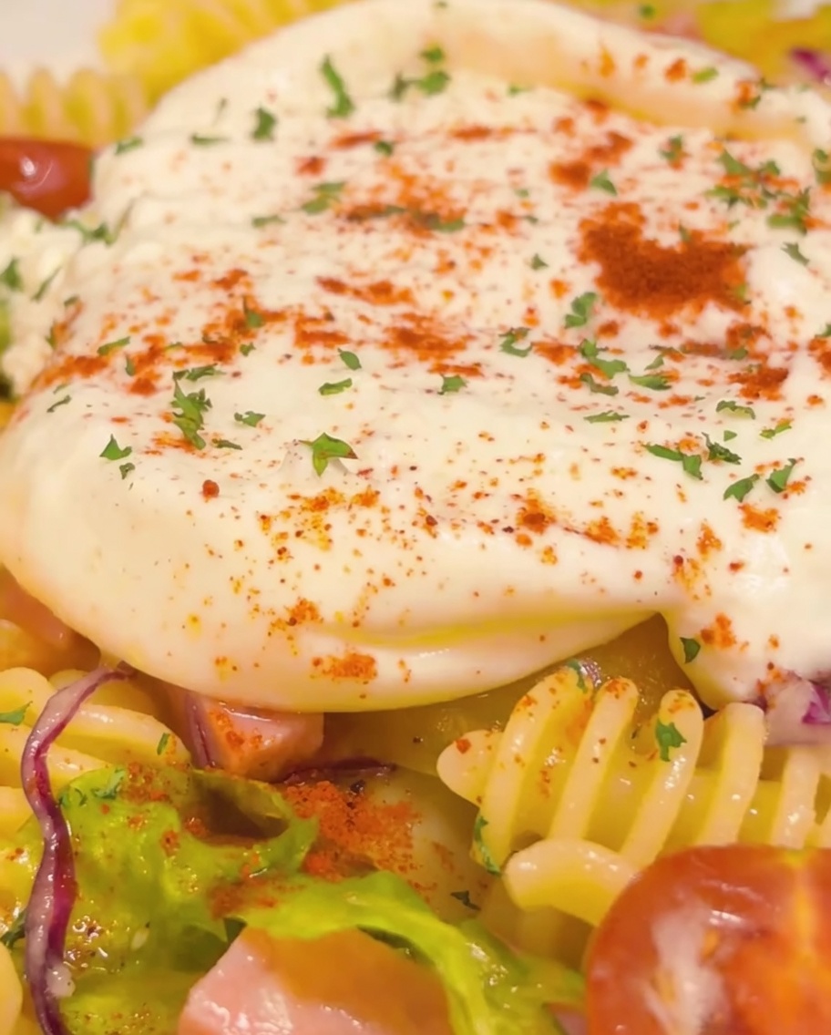 Primo piano del piatto di pasta finito con centro di burrata, guarnito con prezzemolo e peperoncino, con un filo finale di olio doliva.