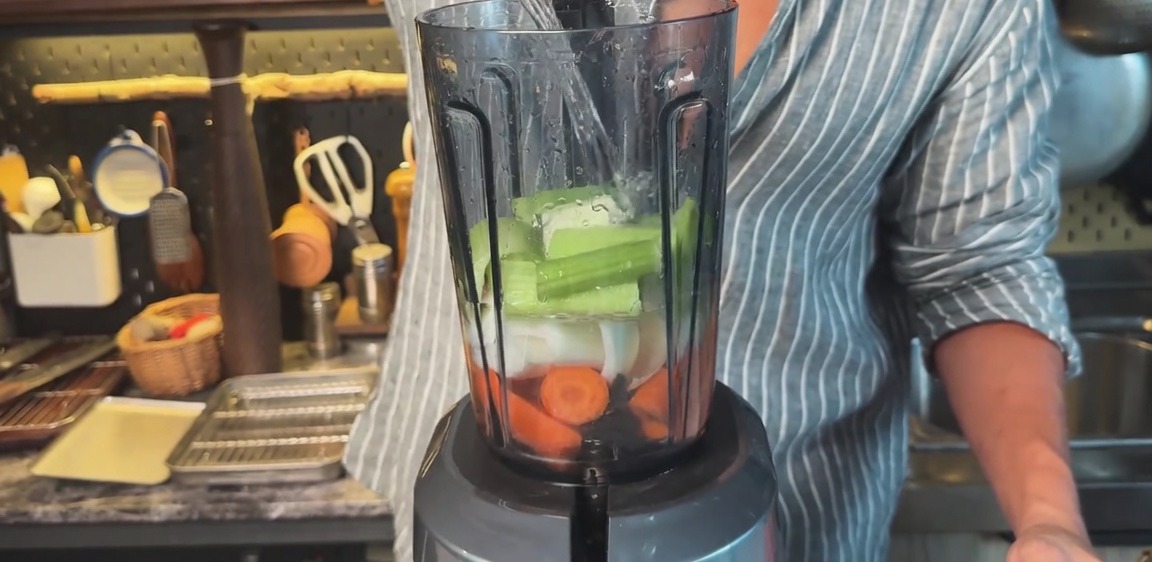 Versare acqua in un frullatore riempito con carote, cipolle e sedano tritati.