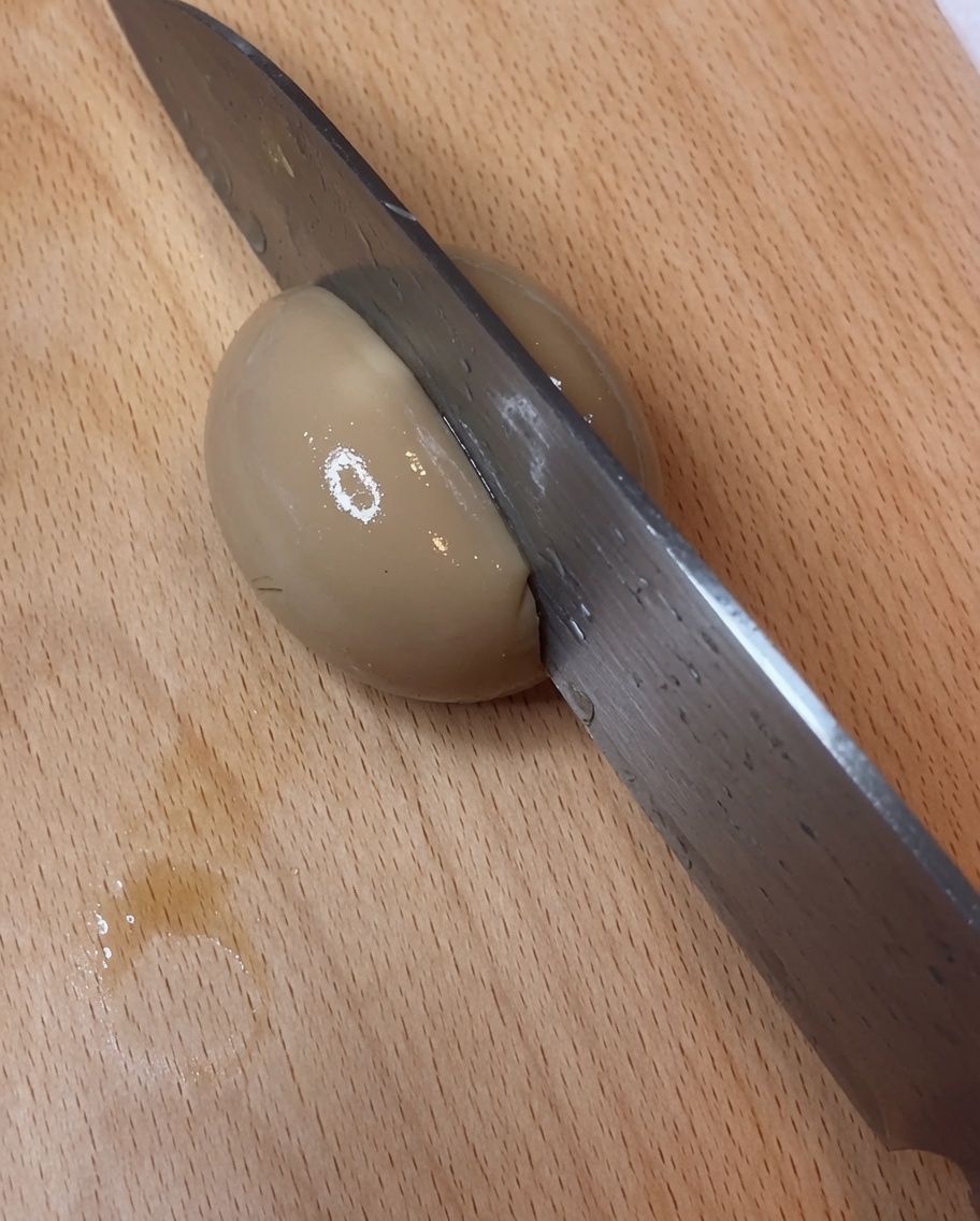 Un uovo marinato alla soia diviso perfettamente a metà su un tagliere, mostrando un tuorlo vivace e fondente.