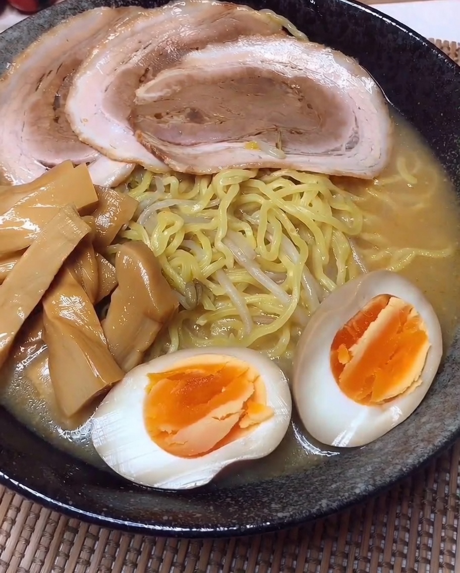 Una ciotola di ramen composta con file ordinate di maiale a fette, germogli di bambù e metà di uova marinate.