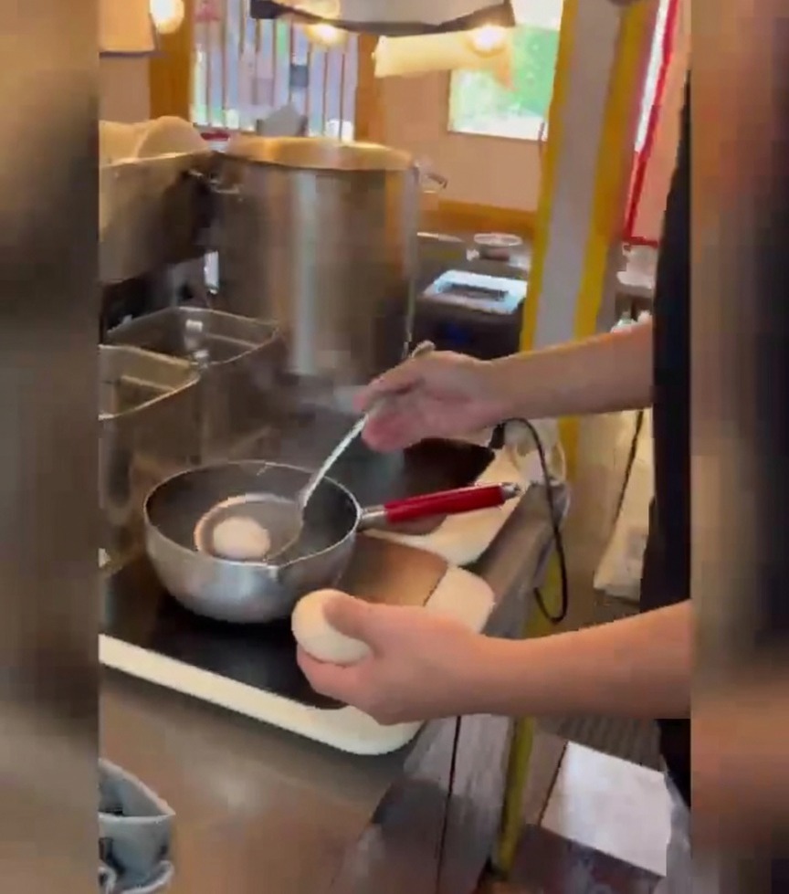 Una persona usa un colino a rete per immergere delicatamente delle uova bianche in una pentola di acqua bollente.