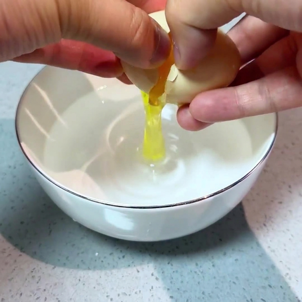 Due mani che rompono con cura un uovo fresco in una ciotolina dacqua.