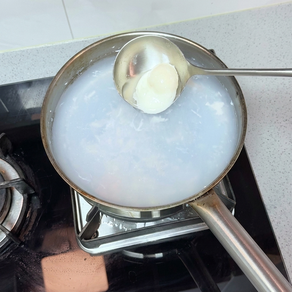 Un mestolo che preleva un uovo in camicia dallacqua bollente.