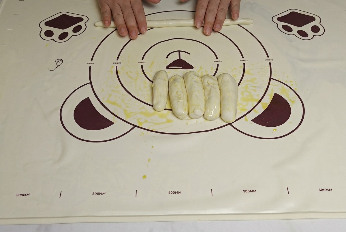 Mani che allungano le strisce di impasto oliato sul tappetino per renderle più lunghe e sottili.