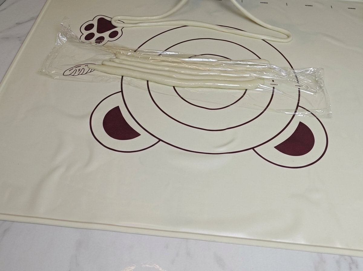 Mani che tirano con cura una striscia di impasto preparato per ottenere un noodle uniforme.