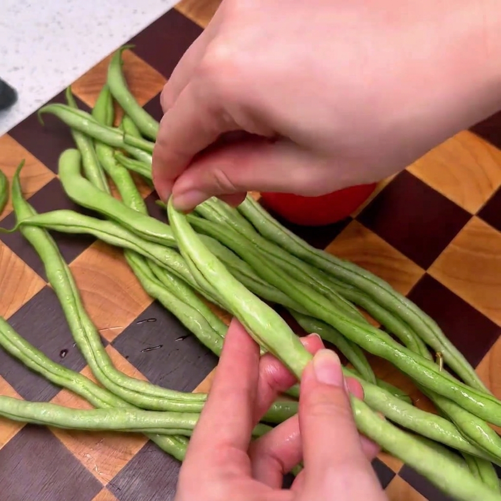 Fagiolini che vengono puliti su un tagliere in legno a scacchi.