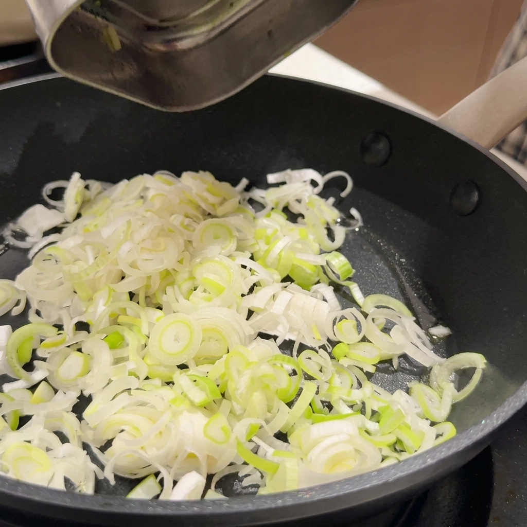 Cipollotti affettati e aglio tritato che sfrigolano in olio in una padella antiaderente.