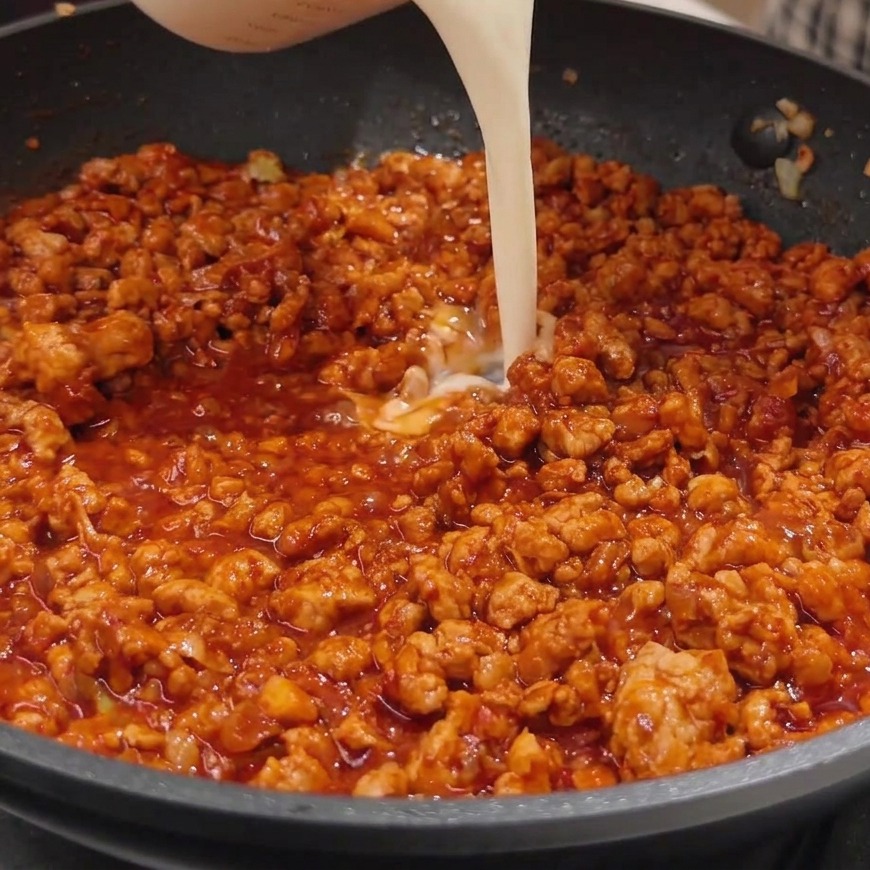 Latte di soia bianco versato da un misurino in una padella con il sugo di miso e carne.