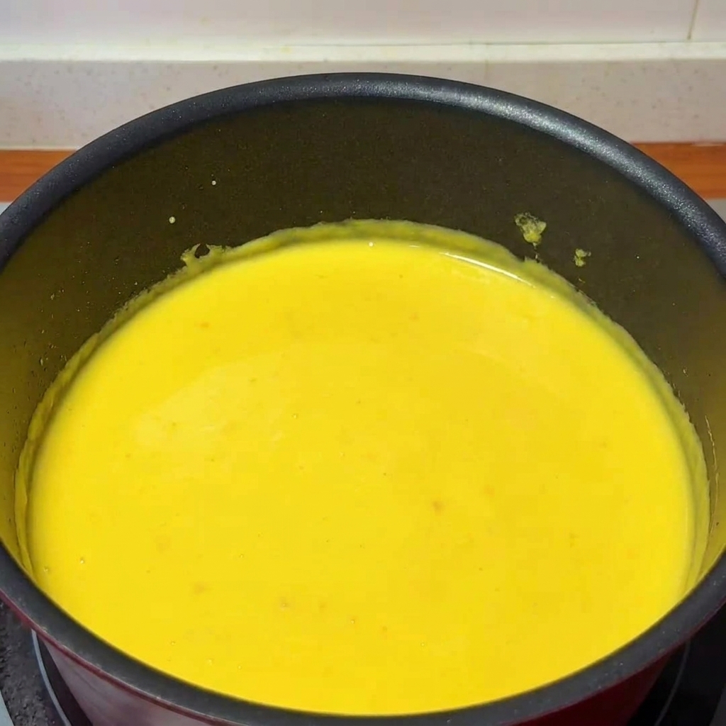 Un mestolo versa il succo di yuzu fresco in un pentolino contenente una densa salsa al formaggio, mescolata da un cucchiaio di legno.