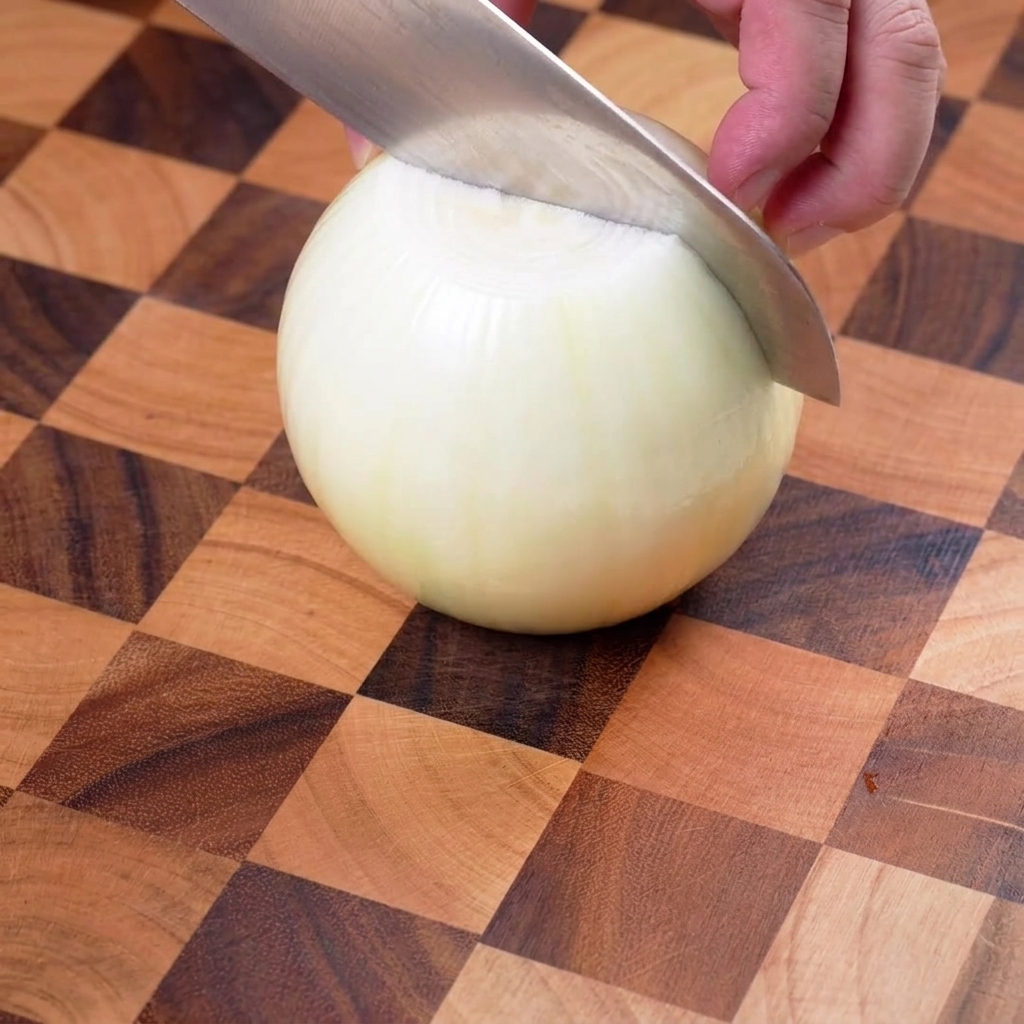 Cipolla dorata tagliata con cura in strisce sottili su un tagliere di legno.