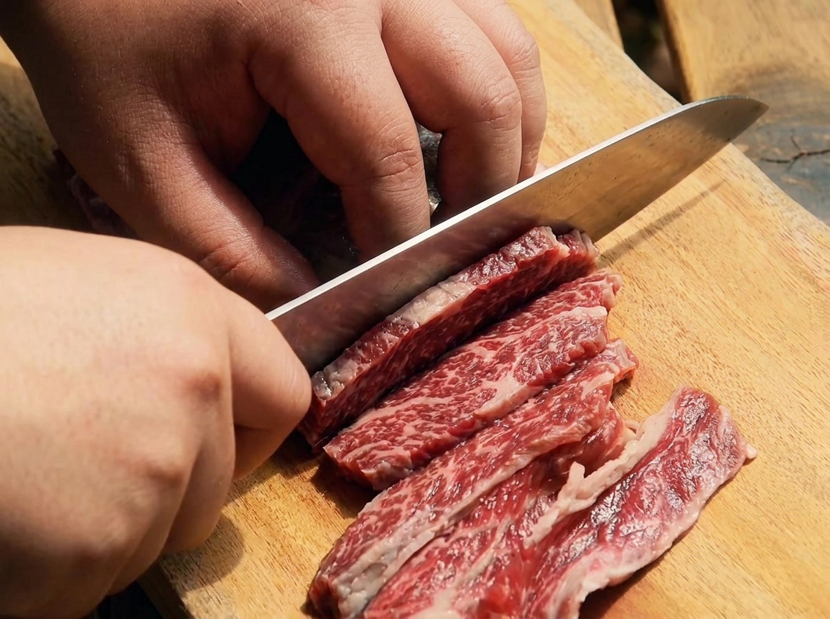 Un coltello affilato che taglia le costine di manzo crude a striscioline sottili su un tagliere di legno.