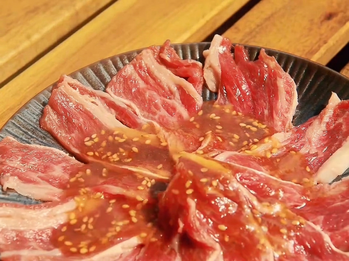 Fette sottili di manzo crudo disposte in un piatto basso, ricoperte dalla salsa Yakiniku appena preparata.