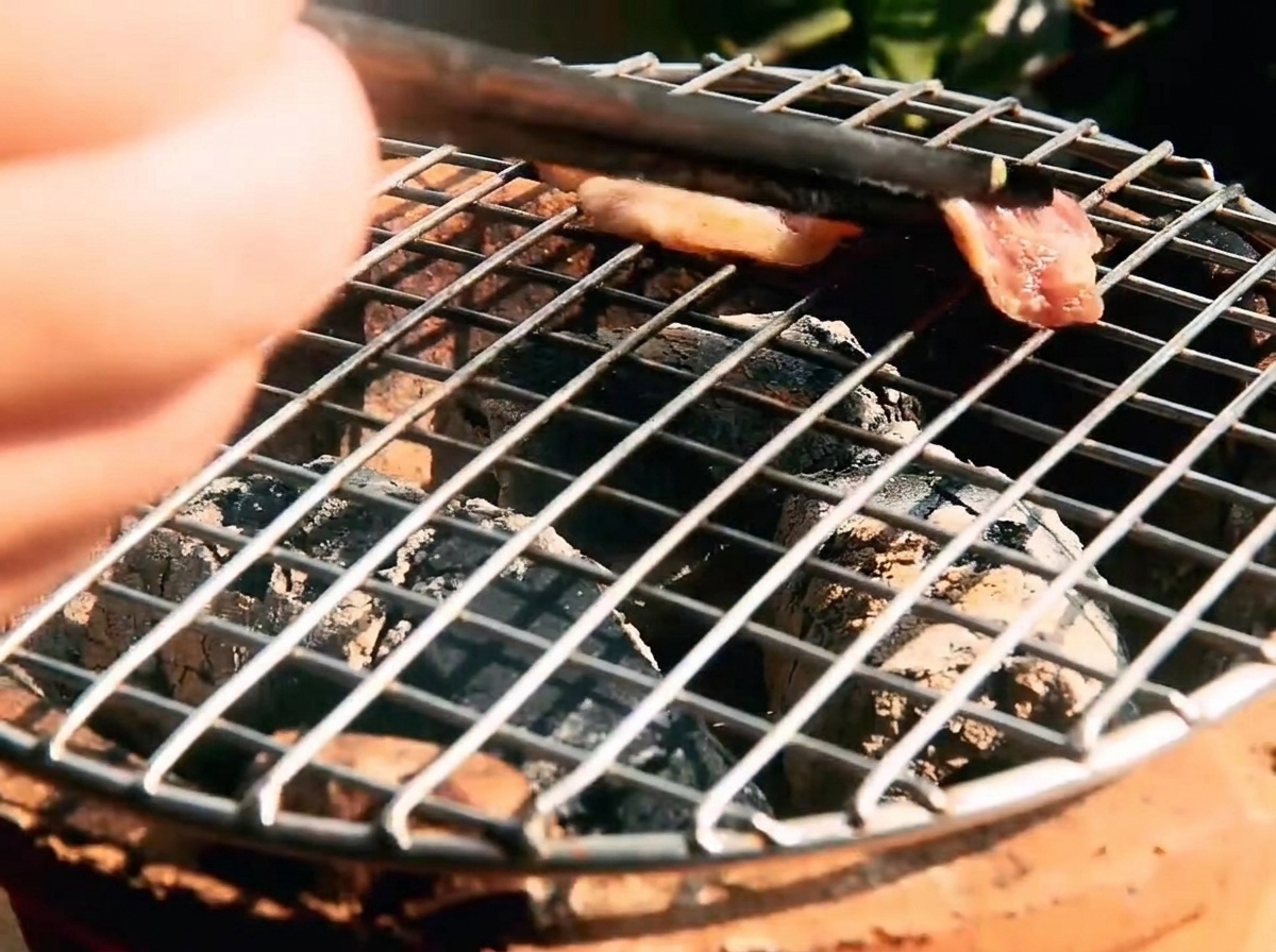 Strisce di manzo marinato in cottura su una griglia rovente con carboni ardenti visibili al di sotto.