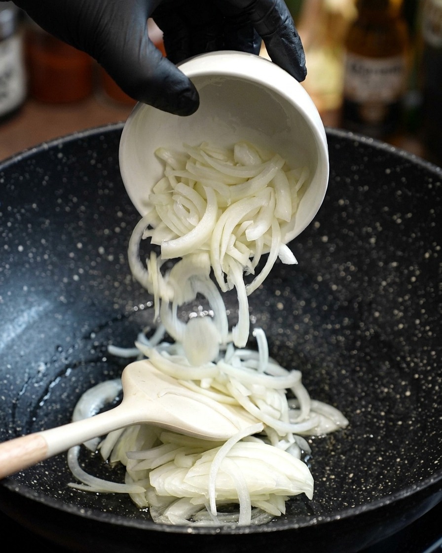 Cipolle bianche affettate aggiunte in padella con olio caldo e mescolate con una spatola.