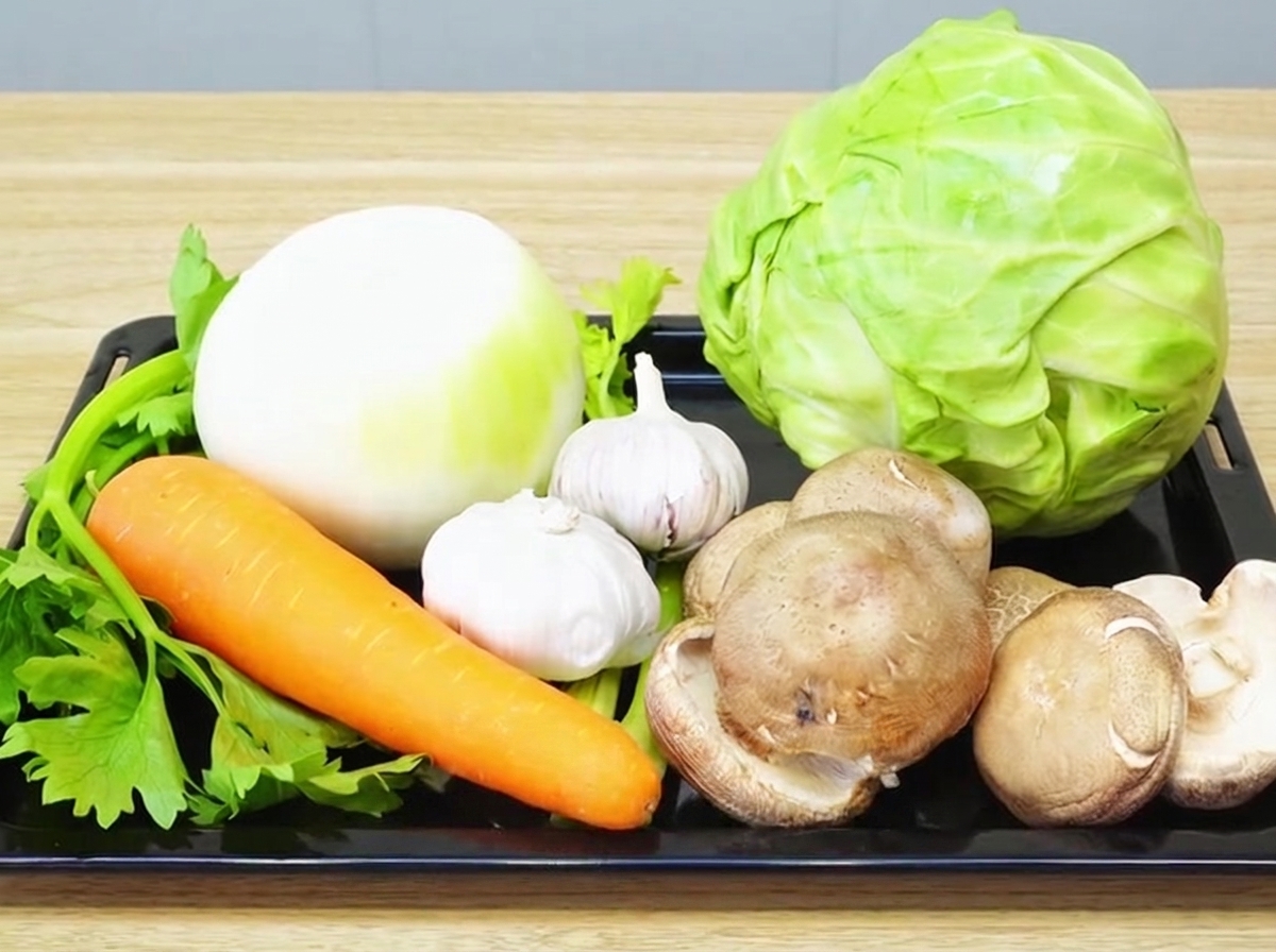 Una varietà di verdure fresche tra cui cipolla, aglio, carota, sedano, shiitake e cavolo, disposte ordinatamente su un tagliere di legno.