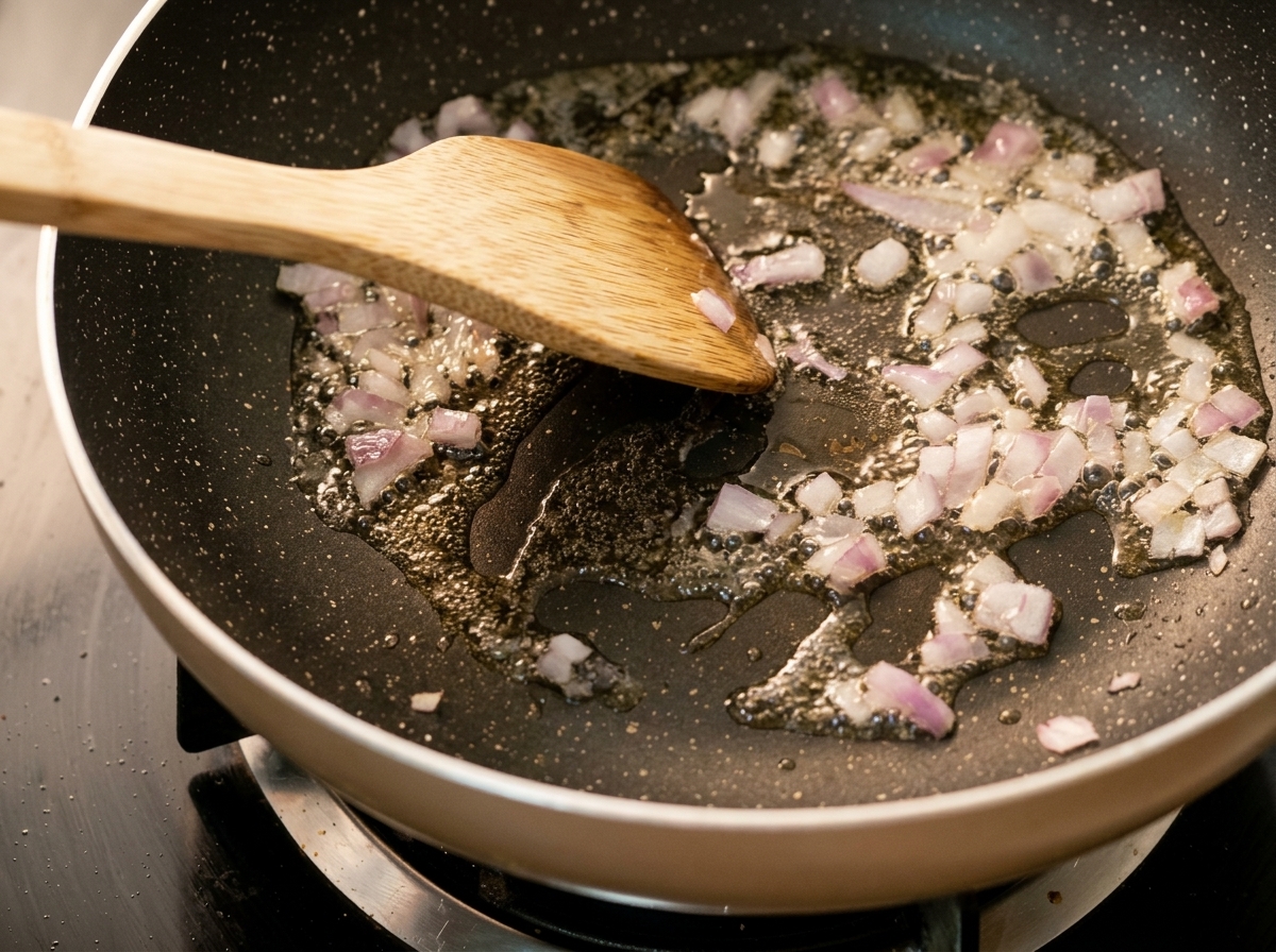 Cipolle tritate che cuociono in una padella calda con olio, mescolate con una spatola di legno.