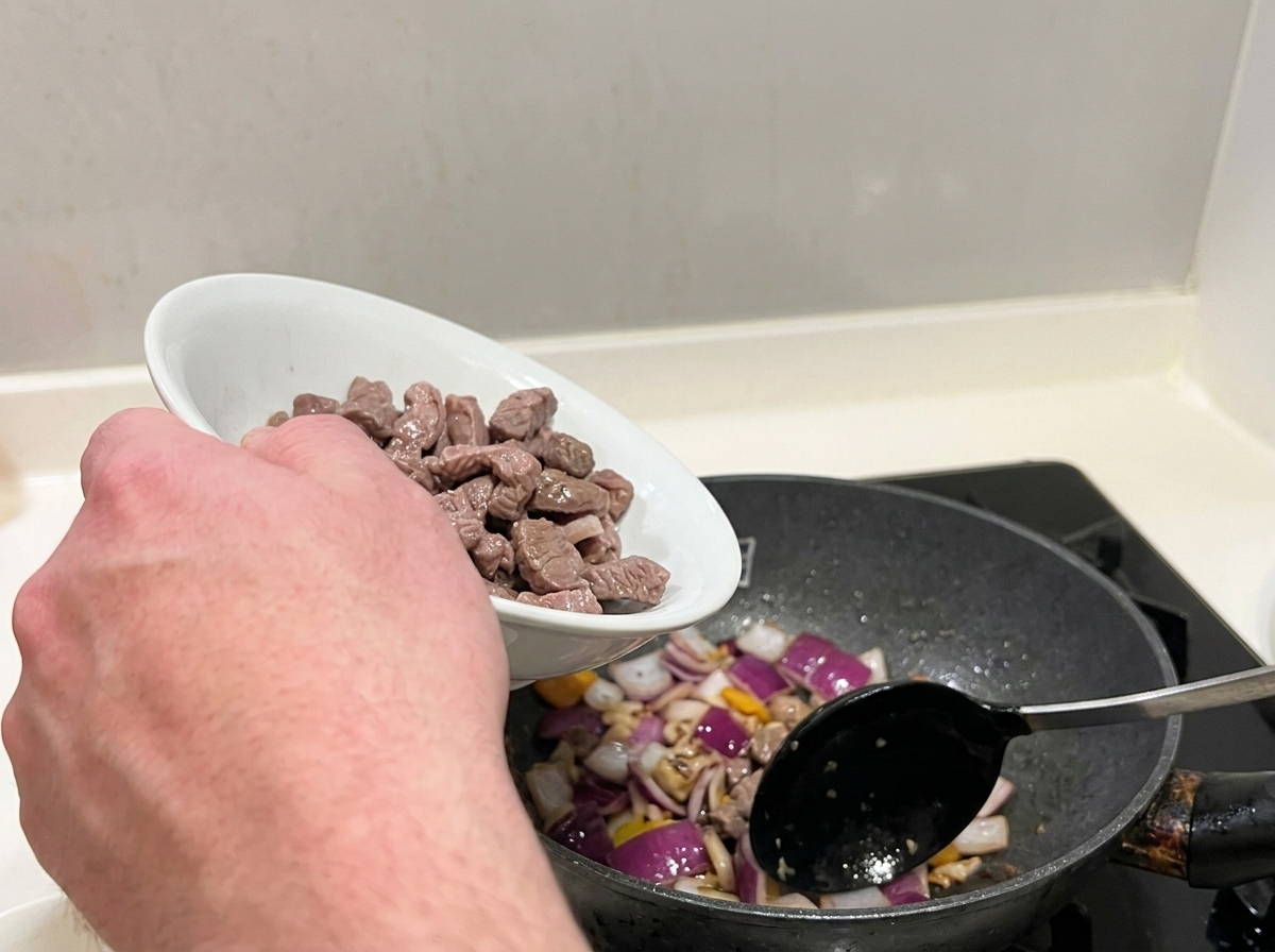 Bocconcini di manzo sbollentati mescolati con cipolle rosse soffritte in padella.