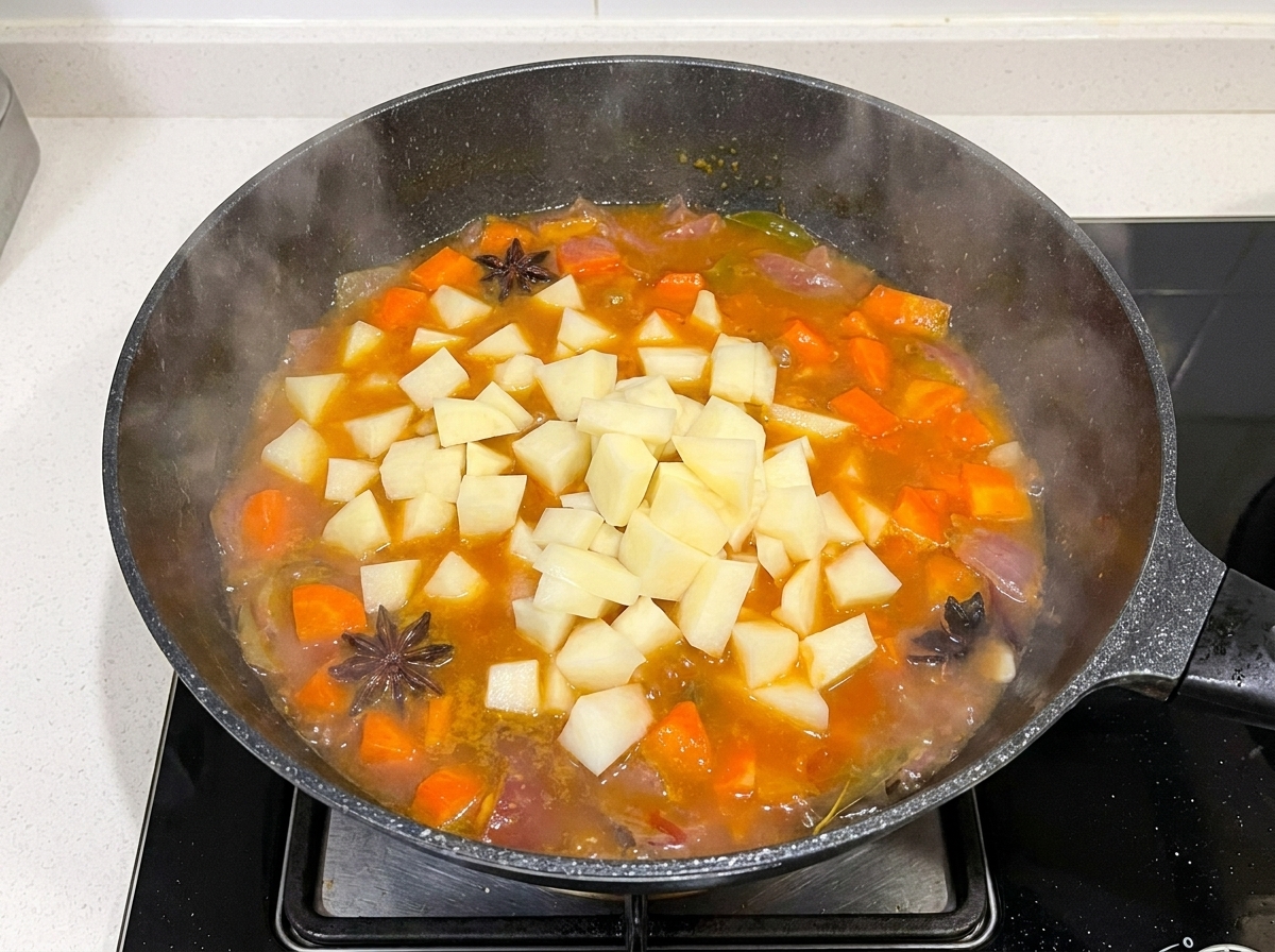 Patate a dadini aggiunte in una padella contenente brodo di manzo, carote e cipolle in ebollizione.