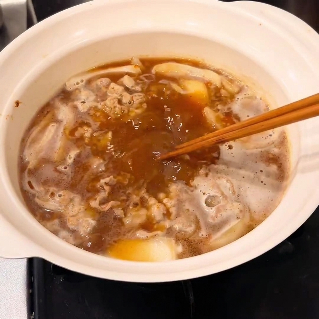 Un blocco di roux per curry mescolato nella pentola per addensare la salsa.