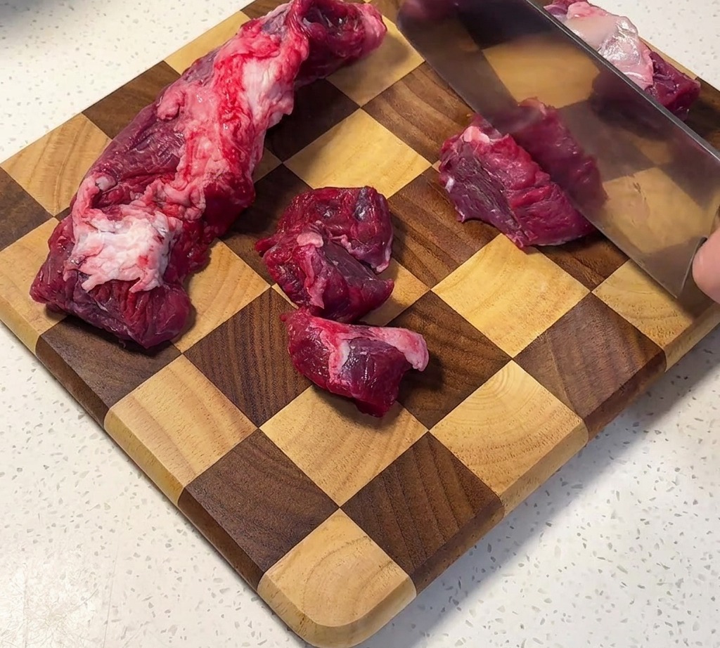 Punta di petto di manzo tagliata a cubetti uniformi su un tagliere in legno.