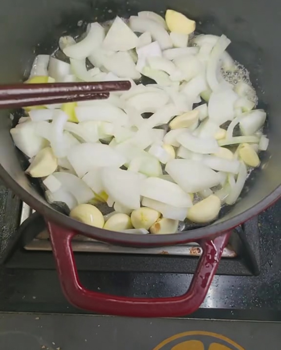 Soffriggere pezzi di cipolla e aglio in una pentola con le bacchette.