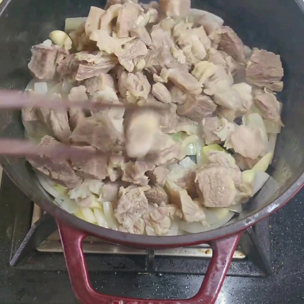 Mescolare cubetti di manzo sbollentati con cipolla e aglio in una padella.