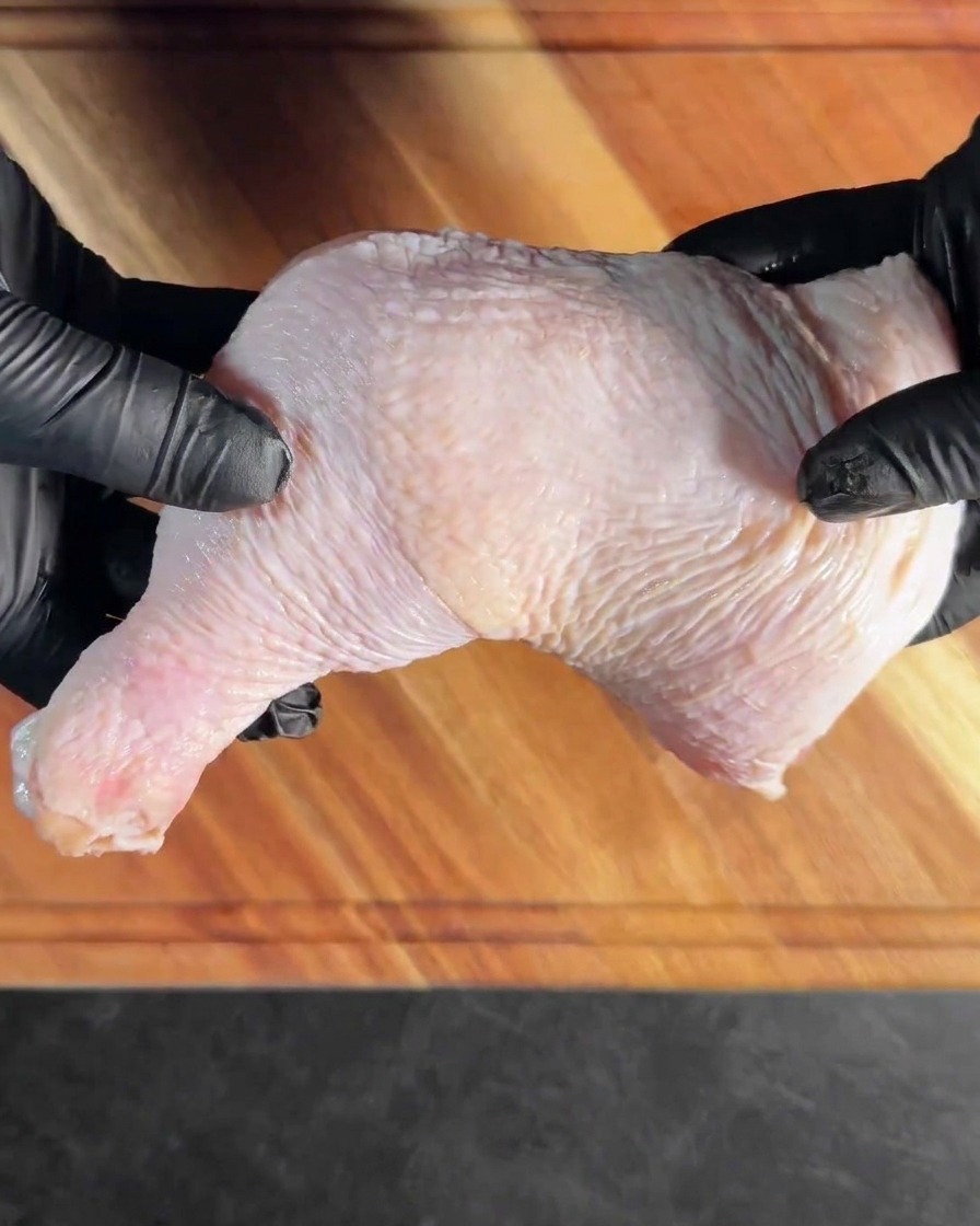 Una coscia di pollo disossata stesa su un tagliere di legno.