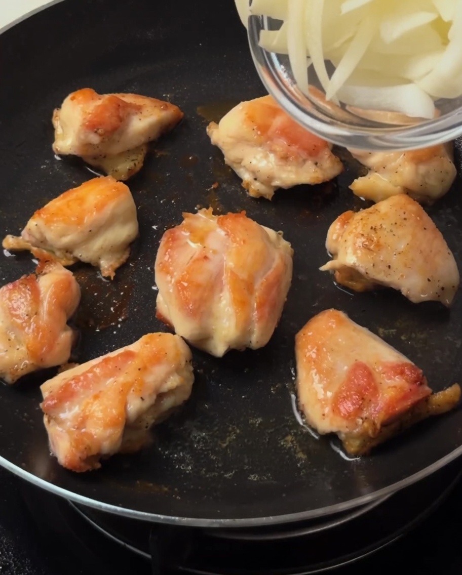 Cipolle affettate mescolate nella padella insieme ai bocconcini di pollo dorati.