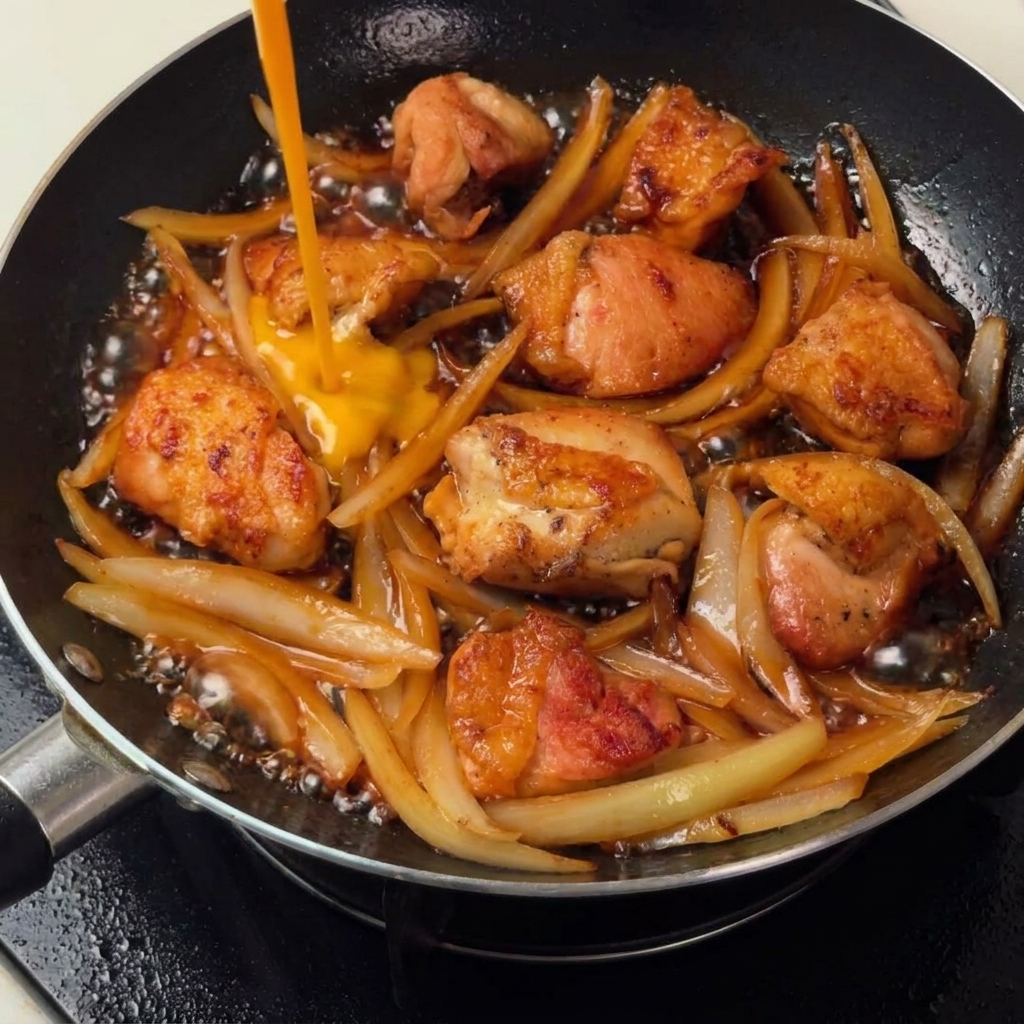 Uova sbattute versate nella padella sopra il mix di pollo e cipolla.
